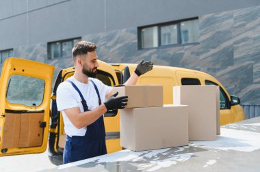 Eldiven takan kurye, karton kutuları sarı minibüsünün üstüne yerleştiriyor nakliye ve taşıma için hazırlanıyor.