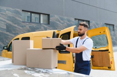 Tulum ve siyah eldivenli kurye, karton kutuları parlak sarı bir teslimat aracına yüklüyor ve verimli bir ulaşım ve lojistik sağlıyor.