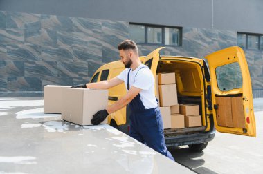 Kurye paketleri sarı bir minibüsün yanındaki başka bir araca yerleştiriyor, güneşli bir şehir caddesinde lojistiği etkili bir şekilde yönetiyor.