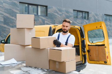 Teslimatçı karton kutuları dikkatlice ticari bir minibüse yerleştiriyor, sevkiyat ve dağıtıma hazırlanıyor.