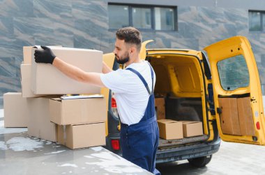 Eldiven giyen kurye, karton kutuları verimli bir nakliye ve lojistik için parlak sarı bir teslimat aracına yüklüyor.