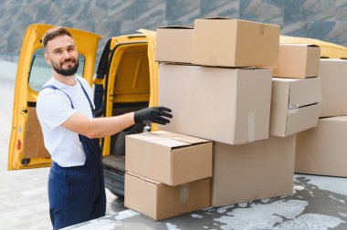 Eldiven takan kurye, karton kutuları dikkatlice parlak sarı bir teslimat kamyonunun üstüne yerleştiriyor, verimli nakliye ve lojistik için hazırlanıyor.