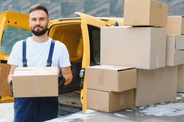 Karton kutularla dolu, kargo ve teslimat için hazır sarı bir minibüsün yanında eldiven taşıyan bir kurye.