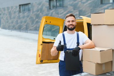 Karton kutularla dolu sarı minibüsünün yanında yaptığı işten memnuniyet duyan bir kurye.