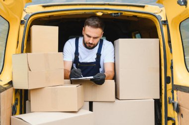 Karton kutuları bir teslimat kamyonunda kontrol ederken, karton panoya kurye yazması, malların nakliyesi ve taşınması için hazırlanıyor