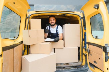 Kontrol listesini tutarken ve karton kutularla dolu bir karavanda otururken kurye, hızlı teslimat ve paket sevkiyatı kavramı