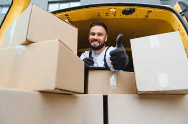 Kurye pano tutuyor ve karton kutularla çevrili bir şekilde hareket ediyor.