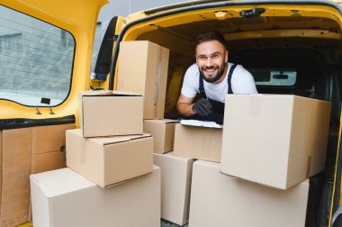 Karton kutularla dolu minibüsün içindeki paketleri kontrol ederken gülümseyen dağıtım sürücüsü panoya yazı yazıyor