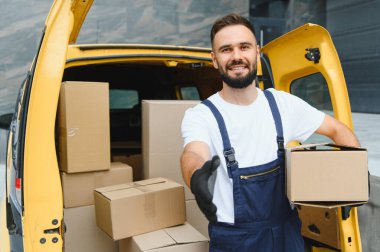 Karton kutuyu tutarken el sıkışmak için kurye uzatıyor. Paketlerle dolu açık teslimat kamyonetinin yanında duruyor.
