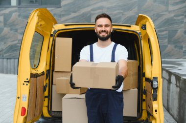Eldivenli kurye, elinde bir paket, içi kutuyla dolu bir teslimat aracının önünde duruyor.
