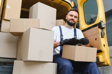 Kurye karton kutuları teslimat minibüsünde kontrol ediyor. Pano kullanıyor, sevkiyat ve teslimatları yönetiyor.
