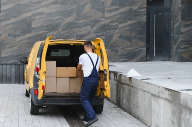 Karton kutuları kargo ve dağıtım için hazırlanan sarı bir karavana yükleyen kurye.