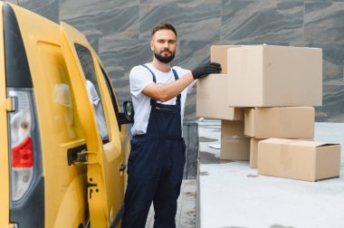 Eldiven takan kurye, parlak sarı bir minibüsün yanına karton kutular yerleştiriyor ve paketler için verimli lojistik malzemeler sağlıyor.
