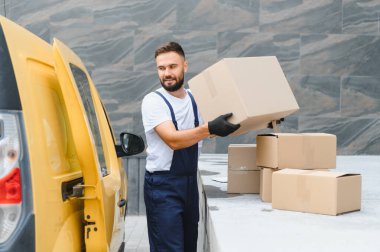 Teslimatçı, parlak sarı bir minibüsten karton kutuları indiriyor, şehrin hareketli sokaklarında etkili bir şekilde malları taşıyor.