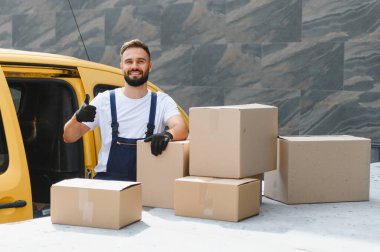Karton kutuları teslimat kamyonetinin üstünde tutarken kurye onay veriyor. Başarılı ve güvenilir bir nakliye hizmeti sunuyor.
