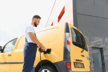 Kurye elektrik dağıtım aracını şarj ediyor, sürdürülebilir ulaşım ve çevre dostu dağıtım hizmetlerini teşvik ediyor