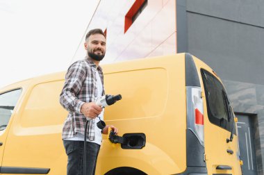 Nakliye şöförü elektrik kamyonunu şarj ediyor, sürdürülebilir ulaşım ve çevre dostu dağıtım hizmetlerini teşvik ediyor