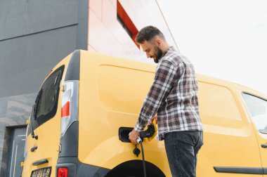 Nakliye şöförü elektrik kamyonunu şarj ediyor, sürdürülebilir ulaşım ve çevre dostu dağıtım hizmetlerini teşvik ediyor