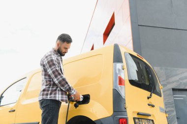 Nakliye şöförü elektrik kamyonunu şarj ediyor, sürdürülebilir ulaşım ve çevre dostu dağıtım hizmetlerini teşvik ediyor