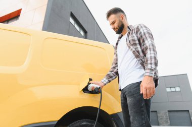 Şehir şarj istasyonunda elektrikli minibüs şarj eden kargo şoförü, sürdürülebilir ulaşım ve çevre dostu teslimat uygulamalarını teşvik ediyor