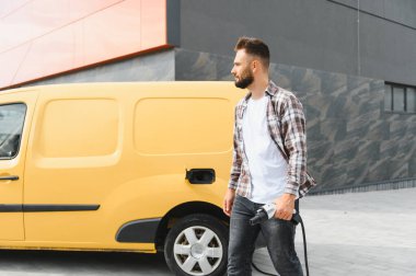 Şarj istasyonunda şarj ettikten sonra sarı bir minibüsten çıkan teslimatçı.