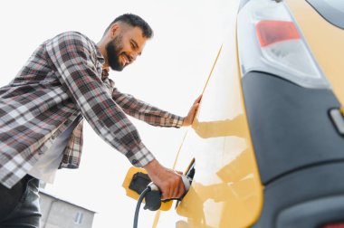 Halka açık bir şarj istasyonunda elektrikli arabasını şarj eden mutlu adam sürdürülebilir ulaşımı kucaklıyor.