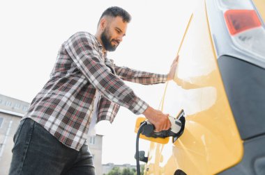 Genç bir adam, halka açık bir şarj istasyonunda elektrikli arabasını şarj ediyor, sürdürülebilir ulaşım ve çevre dostu uygulamaları teşvik ediyor