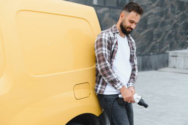 Yükleme kablosu tutan kargo şoförü kalabalık bir şehir ortamında elektrik kamyonunun şarj olmasını bekliyor.