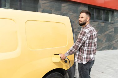 Teslimat şoförü elektrikli minibüsü şarj ediyor, sürdürülebilir ulaşımı teşvik ediyor ve kentsel alanlarda çevre dostu dağıtım hizmetleri sunuyor