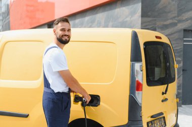 Kurye, elektrik dağıtım aracını şarj ediyor, sürdürülebilir ulaşım ve çevre dostu dağıtım hizmetlerine katkıda bulunuyor
