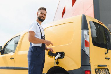 Kurye, elektrik kamyonunun şarj edicisini gösteriyor, sürdürülebilir ulaşımı teşvik ediyor.