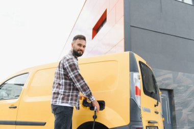 Nakliye şöförü elektrik kamyonunu şarj ediyor, sürdürülebilir ulaşım ve çevre dostu dağıtım hizmetlerini teşvik ediyor