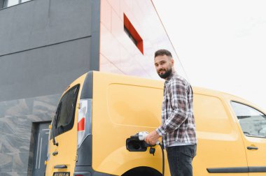 Nakliye şöförü elektrik kamyonunu şarj ediyor, sürdürülebilir ulaşım ve çevre dostu dağıtım hizmetlerini teşvik ediyor