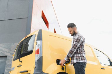 Nakliye şöförü elektrik kamyonunu şarj ediyor, sürdürülebilir ulaşım ve çevre dostu dağıtım hizmetlerini teşvik ediyor