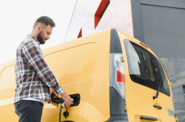 Yükleme istasyonunda elektrik dağıtım minibüsü şarj eden kargo şoförü, sürdürülebilir ulaşım ve çevre dostu dağıtım uygulamalarını teşvik ediyor