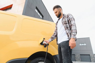 Nakliye şöförü elektrik kamyonunu şarj ediyor, sürdürülebilir ulaşım ve çevre dostu dağıtım hizmetlerini teşvik ediyor