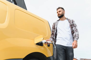 Nakliye şöförü elektrik kamyonunu şarj ediyor, sürdürülebilir ulaşım ve çevre dostu dağıtım hizmetlerini teşvik ediyor