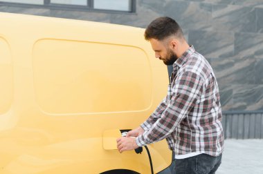 Şehir ortamında elektrik kamyonu şarj eden kargo şoförü, sürdürülebilir ulaşım ve çevre dostu dağıtım hizmetlerini teşvik ediyor