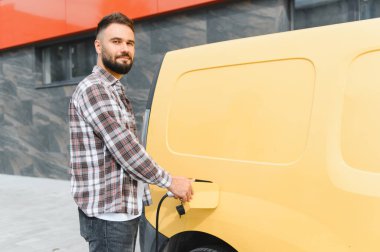 Sürdürülebilir ulaşım ve çevre dostu dağıtım uygulamalarını destekleyen elektrikli minibüsü şarj eden teslimat şoförü