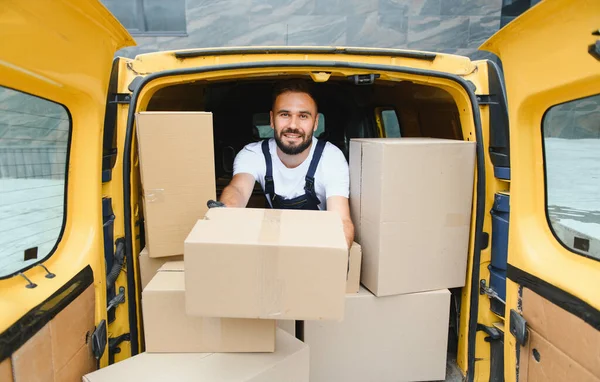 Parlak sarı bir minibüsün karton kutularını taşıyan gülümseyen teslimatçı, şehir lojistiği ve taşımacılığında verimli hizmet sunuyor.