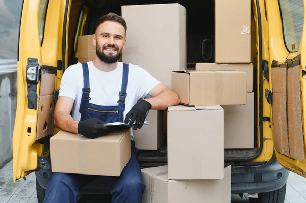 Karton kutulara bakan kurye, sarı bir minibüste elinde bir dosya ve eldiven tutarken...