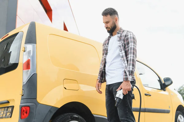 Teslimat şoförü elektrik minibüsünün yanında kablolu yayın tutuyor, sürdürülebilir ulaşım ve çevre dostu dağıtım hizmetlerini destekliyor.