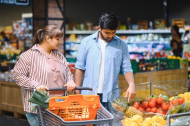 Genç Hintli çift alışveriş arabasını itiyor ve market raflarından taze ürünleri seçiyorlar.