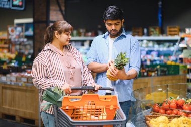 Genç Hintli bir çift, parlak, modern bir süpermarkette alışveriş yaparken olgun bir ananas seçiyor ve birlikte vakit geçiriyorlar.