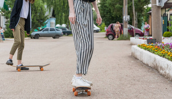 Young girl in a black T-shirt and striped trousers learns to ride a skateboard