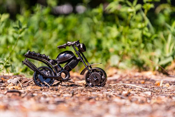 Homemade metal model - a sports motorcycle toy stands on the pavement against an abstract green background