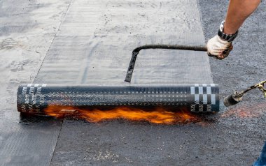İnşaatçı gaz ocağı kullanarak çok katlı bir binanın çatısına su geçirmez malzeme koyuyor. Evin çatısının tadilatı..