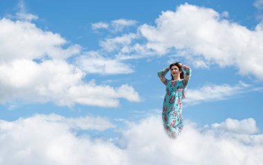 Genç bir kız gökyüzünde yüksek bir bulutun üzerinde duruyor. Yaz eğlencesi kızları.