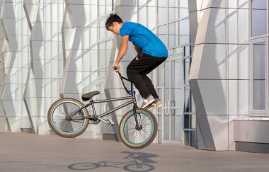 Bmx motorlu genç adam, güzel bir binanın ön cephesinde akrobatik bir gösteri sergiliyor.