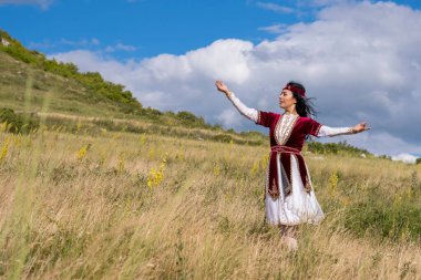 Güzel kırmızı takım elbiseli genç parlak bir kız mavi bir yaz gökyüzüne karşı ulusal bir dans yapıyor.